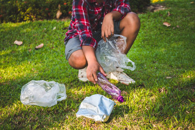 Low section of person collecting garbage on grassy field