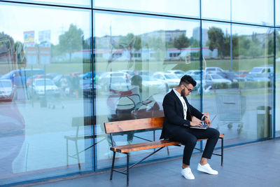 Businessman using digital tablet while sitting on bench outdoors