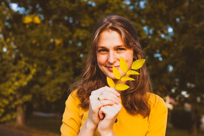 Portrait of woman holding yellow plant against trees