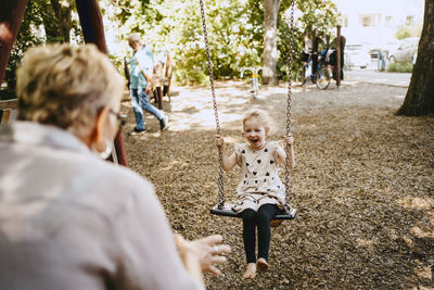 Cheerful girl playing on swing with grandmother at park