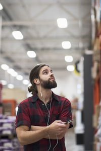 Male customer looking up while listening music through smart phone at hardware store