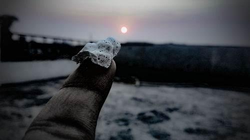 Close-up of human hand against sea during winter