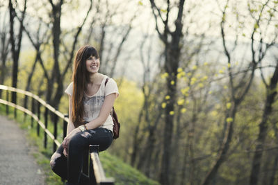 Young woman sitting on railing by road