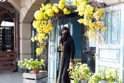 A muslim woman in a beautiful black outfit leaves the store covering her face.