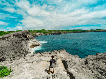 Man standing on rock by sea against sky