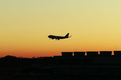 Low angle view of silhouette airplane landing against orange sky