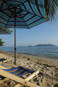 Beach umbrellas and lounge chairs by sea against sky