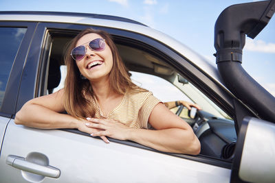 Happy woman wearing sunglasses looking through car window