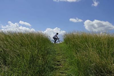 Man cycling on field  against sky