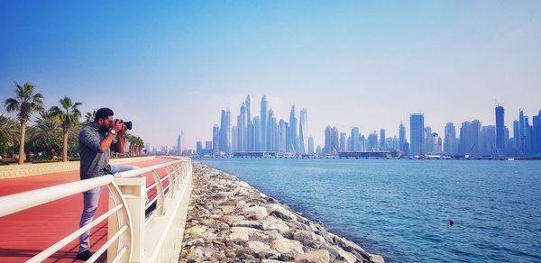 Man standing on sea by buildings against clear sky