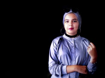 Portrait of teenage girl standing against black background