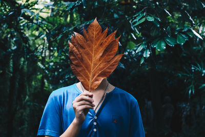 Young man covering face with autumn leaf against plants