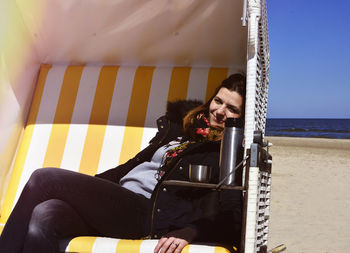 Young woman resting in yellow hooded beach chair on sea shore during sunny day