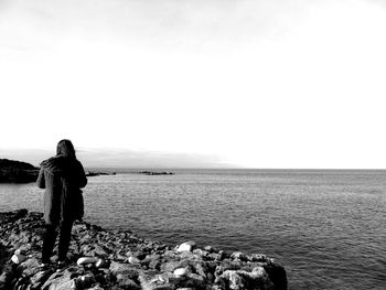 Rear view of woman standing at beach against clear sky