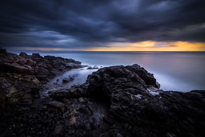 Rock formations by sea against cloudy sky during sunset