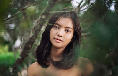 Portrait of beautiful young woman by trees