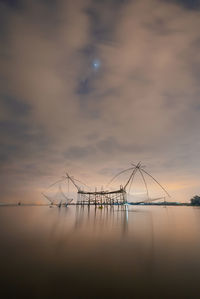 Cranes in sea against sky during sunset