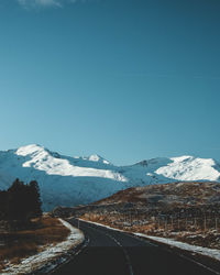 Road leading towards snowcapped mountains against clear sky