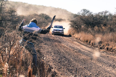 People on dirt road by trees against sky