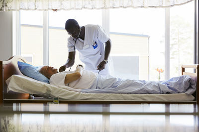 Male nurse examining senior man lying on bed in brightly lit hospital