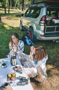 High angle view woman playing musical instrument while sitting by friend in camp