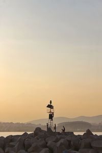 People standing on rock by sea against sky during sunset