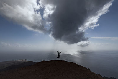 Silhouette man jumping by sea against sky