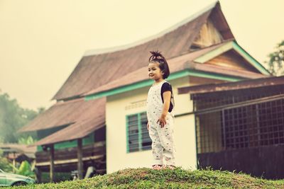 Cute girl standing on field against house