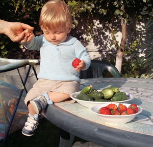 Baby boy with food in plates sitting on table in yard