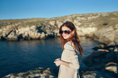 Portrait of young woman wearing sunglasses standing on rock