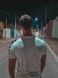 Rear view of man standing on road at night