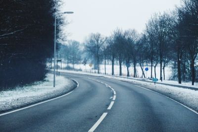 Road by trees against sky during winter