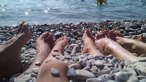 Low section of person relaxing on pebbles at sea shore
