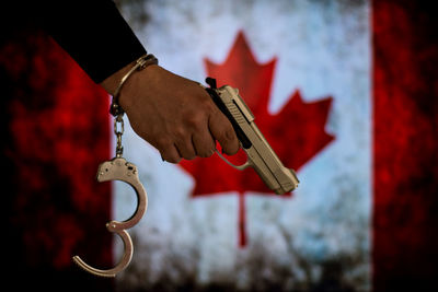 Close-up of criminal holding gun against canadian flag