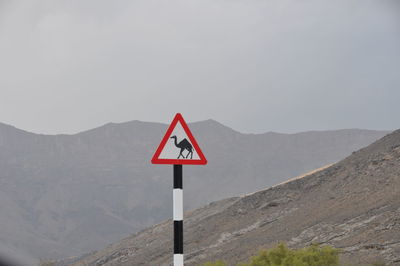 Road sign by mountains against sky