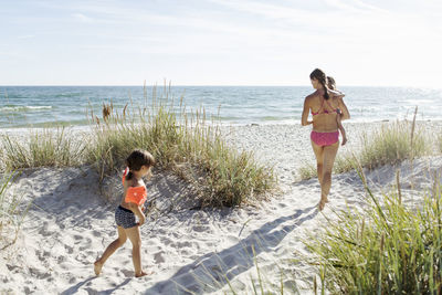 Mother with daughters walking on beach against sky during sunny day