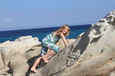 Portrait of cute girl climbing on rock formation at beach