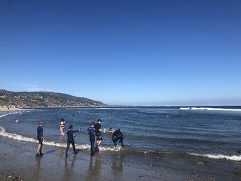 People on beach against clear blue sky