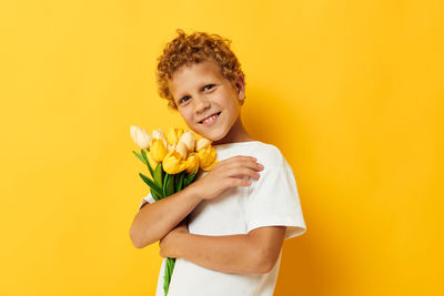 Portrait of girl holding yellow flower against orange background