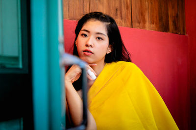 Portrait of beautiful young woman standing against yellow wall