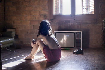 Rear view of shirtless woman sitting on wooden floor at room