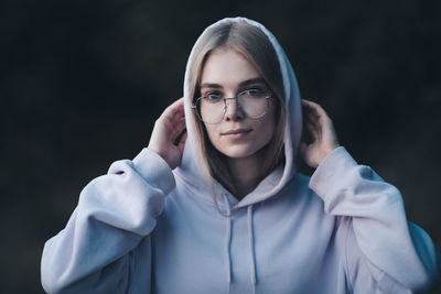 Cute teenage student girl 17-18 year old wear glasses and pink hoody in dark outdoor close up