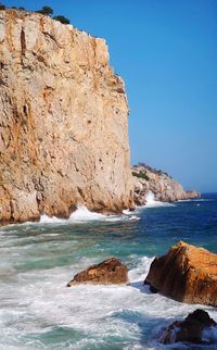 Scenic view of rocks by sea against clear blue sky