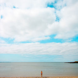 Rear view of girl standing at beach against cloudy sky