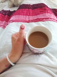 Midsection of woman with coffee cup on bed