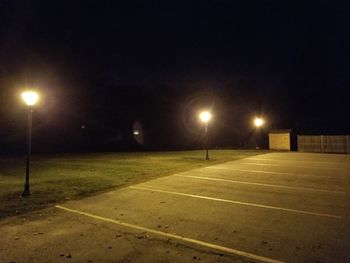 Illuminated street lights against sky at night