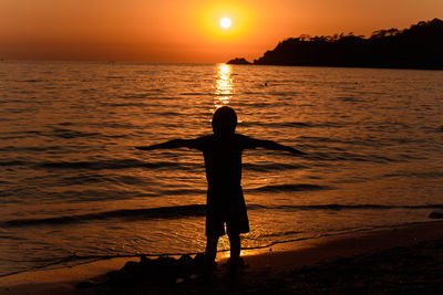 Silhouette person standing on beach during sunset