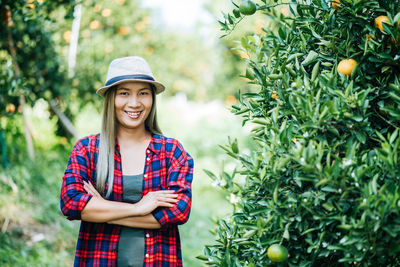 Portrait of smiling woman standing by orange tree in orchard