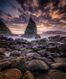 Rocks on beach against sky during sunset