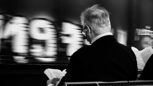 Rear view of man reading and waiting for the train in city